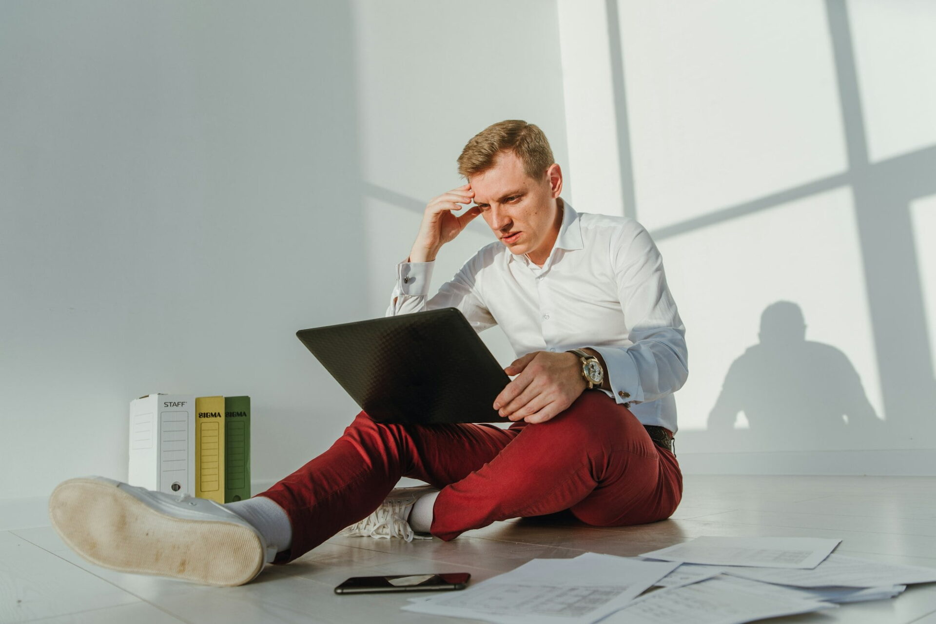 A young businessman working on a laptop and with papers the expression of the face in confusion - Image from Inkfire Limited